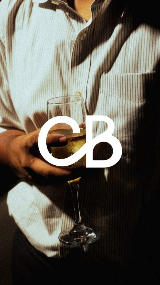 Person in a striped shirt holding a glass of white wine, with the Ciao Bacco CB monogram over the frame