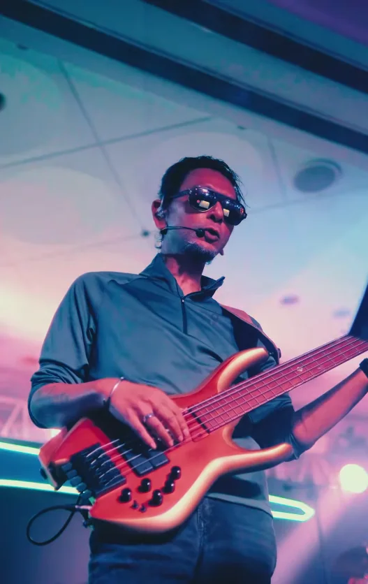 Bass guitarist in sunglasses performing under pink and teal stage lighting
